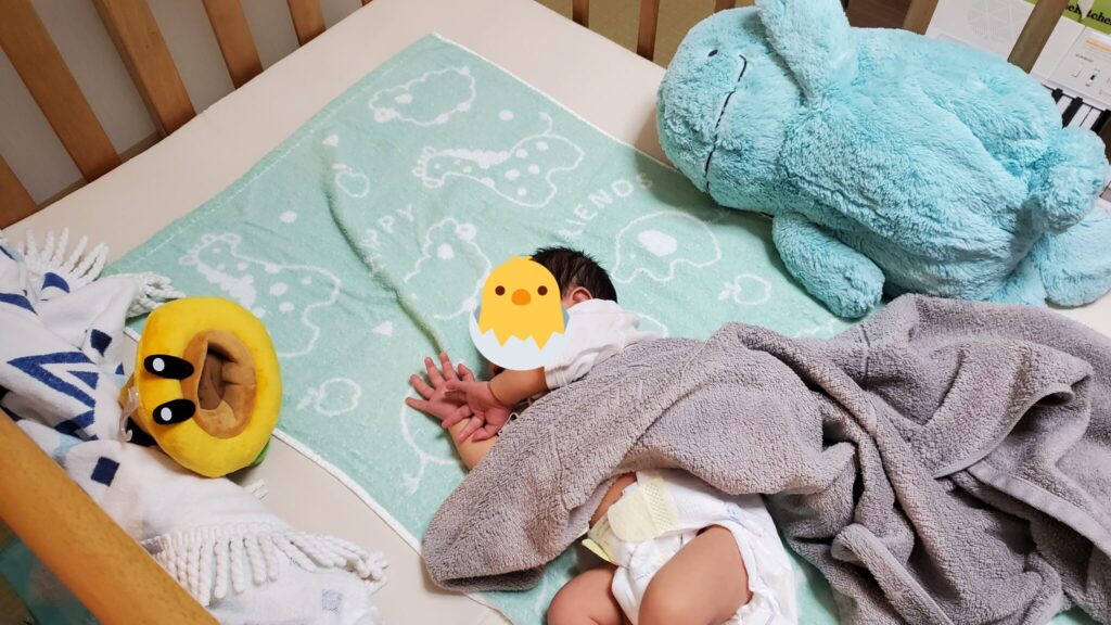 ベビーベッドの上でぬいぐるみや布団に囲まれる我が子